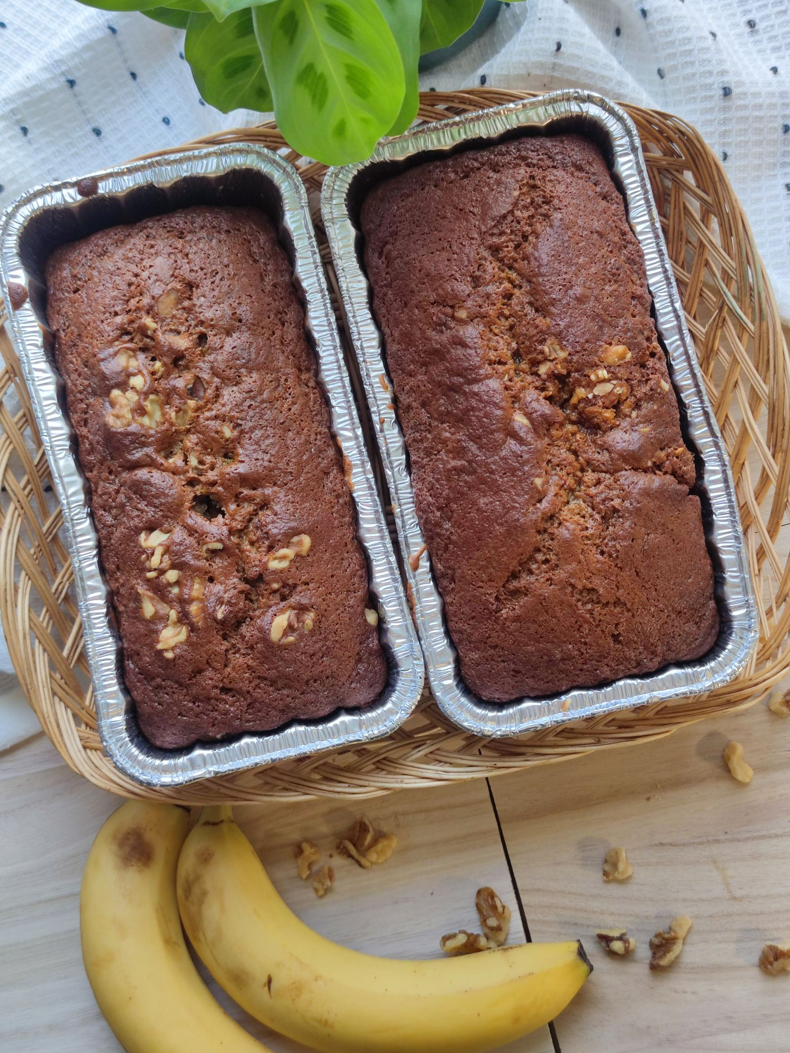 Two fresh homemade walnut banana bread loaves in foil pans with ripe bananas