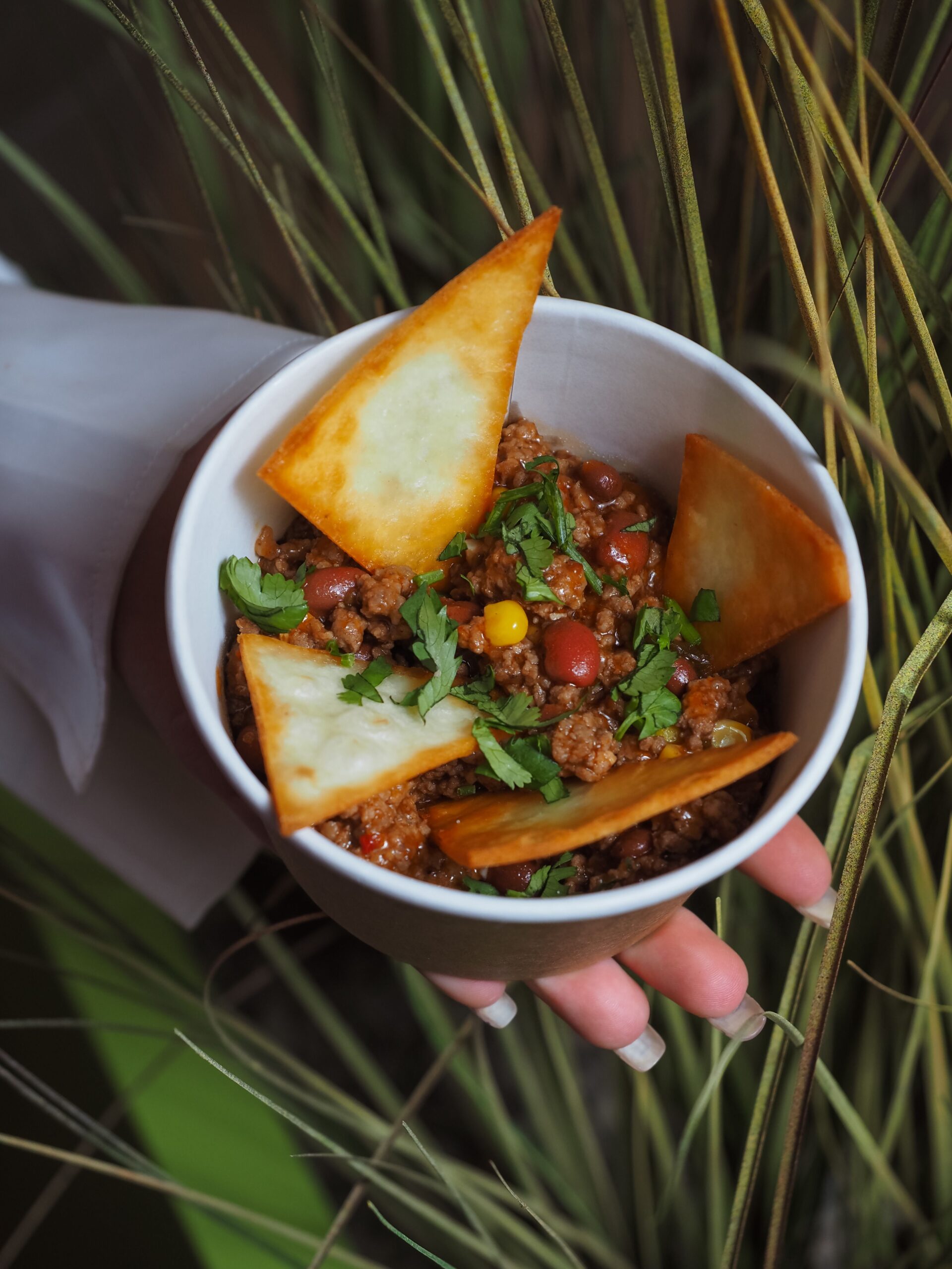 A bowl of beef chili topped with crispy tortilla chips and coriander