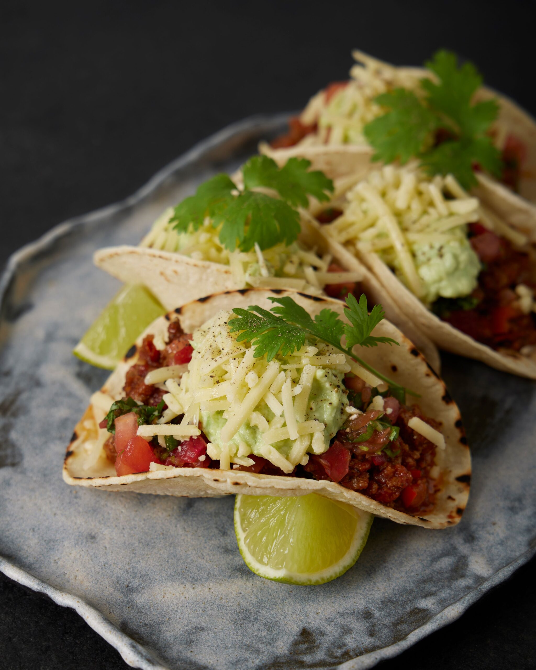 Ground beef tacos topped with cheese, salsa and cilantro, with lime wedges