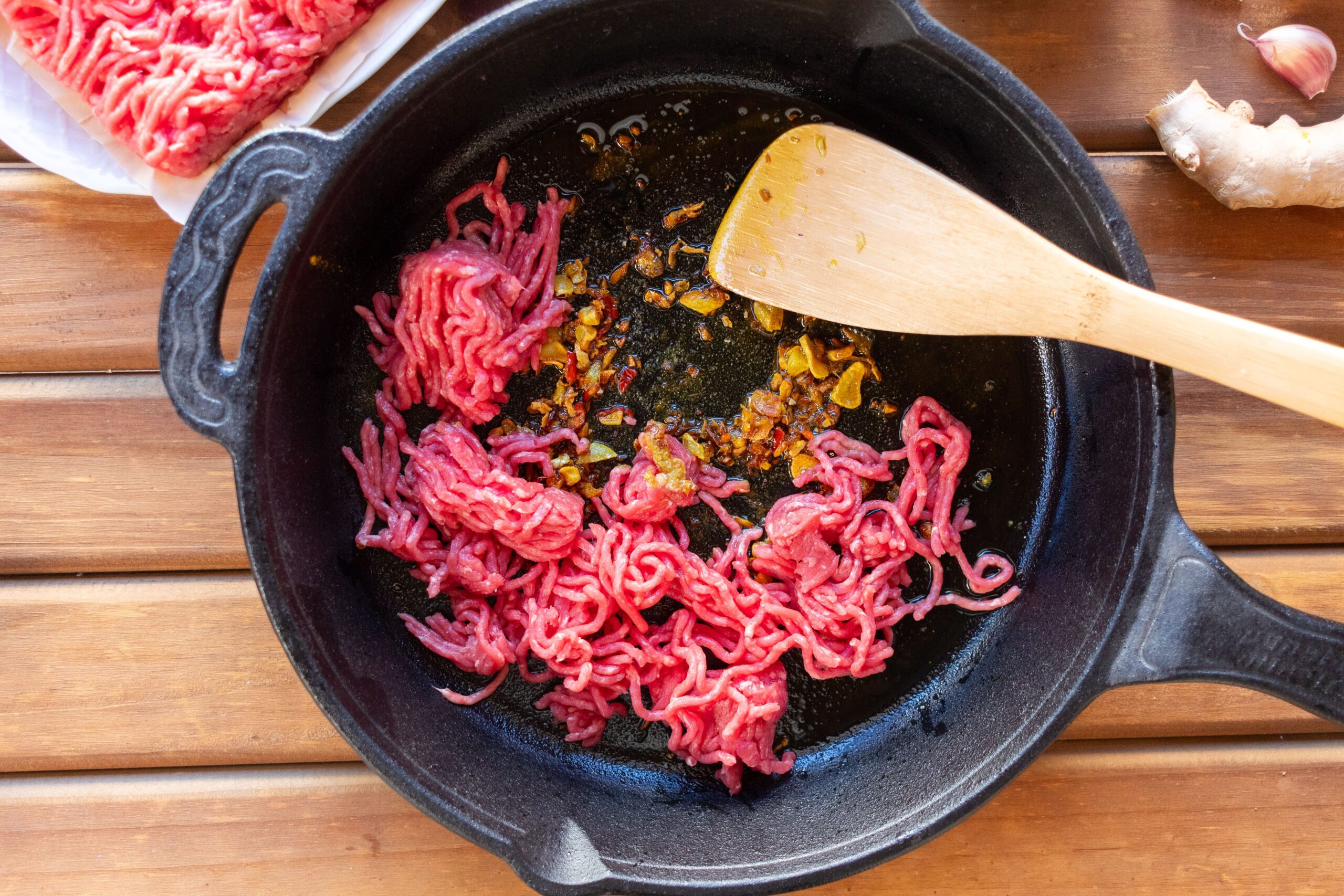 Ground beef browning in a cast iron skillet with garlic