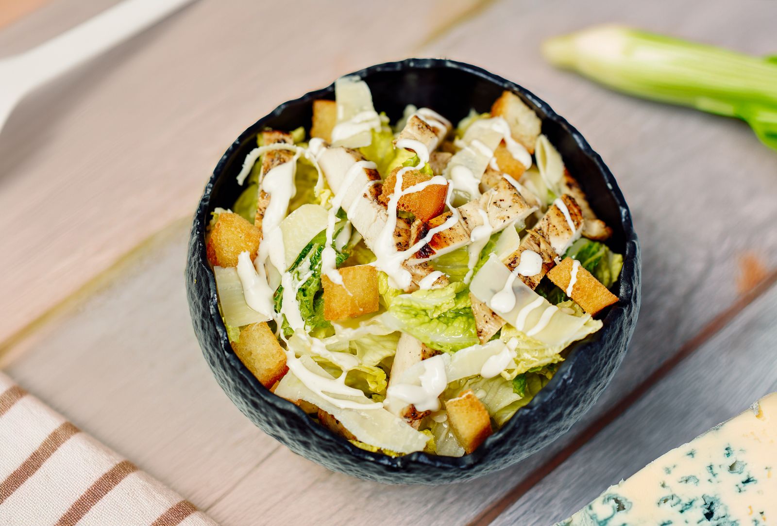 High angle view of a Caesar salad with grilled chicken and croutons in a black bowl