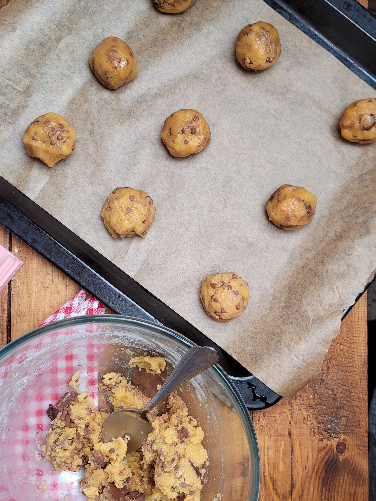 Freshly rolled chocolate chip cookie dough balls spaced on a parchment-lined tray, ready to bake
