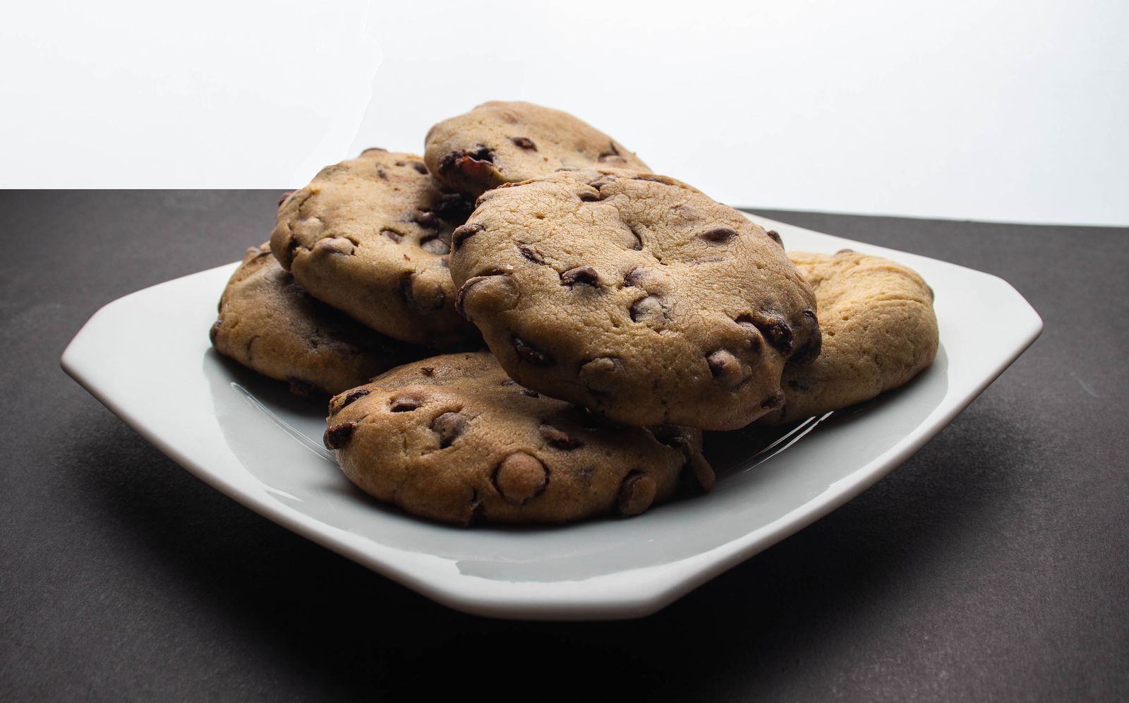 Stack of chewy chocolate chip cookies with crisp edges on a white plate