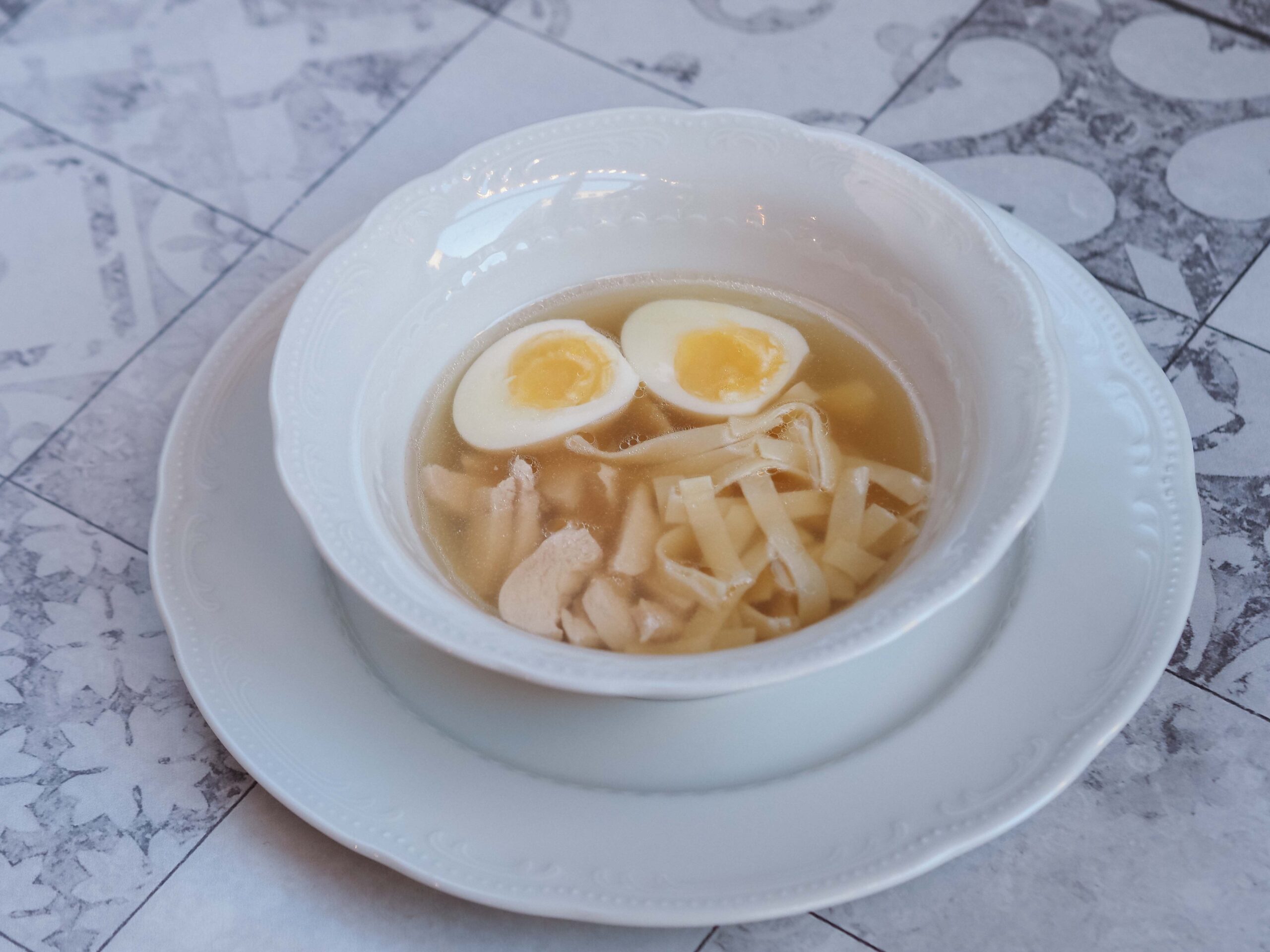Chicken noodle soup served in a white bowl with sliced egg garnish