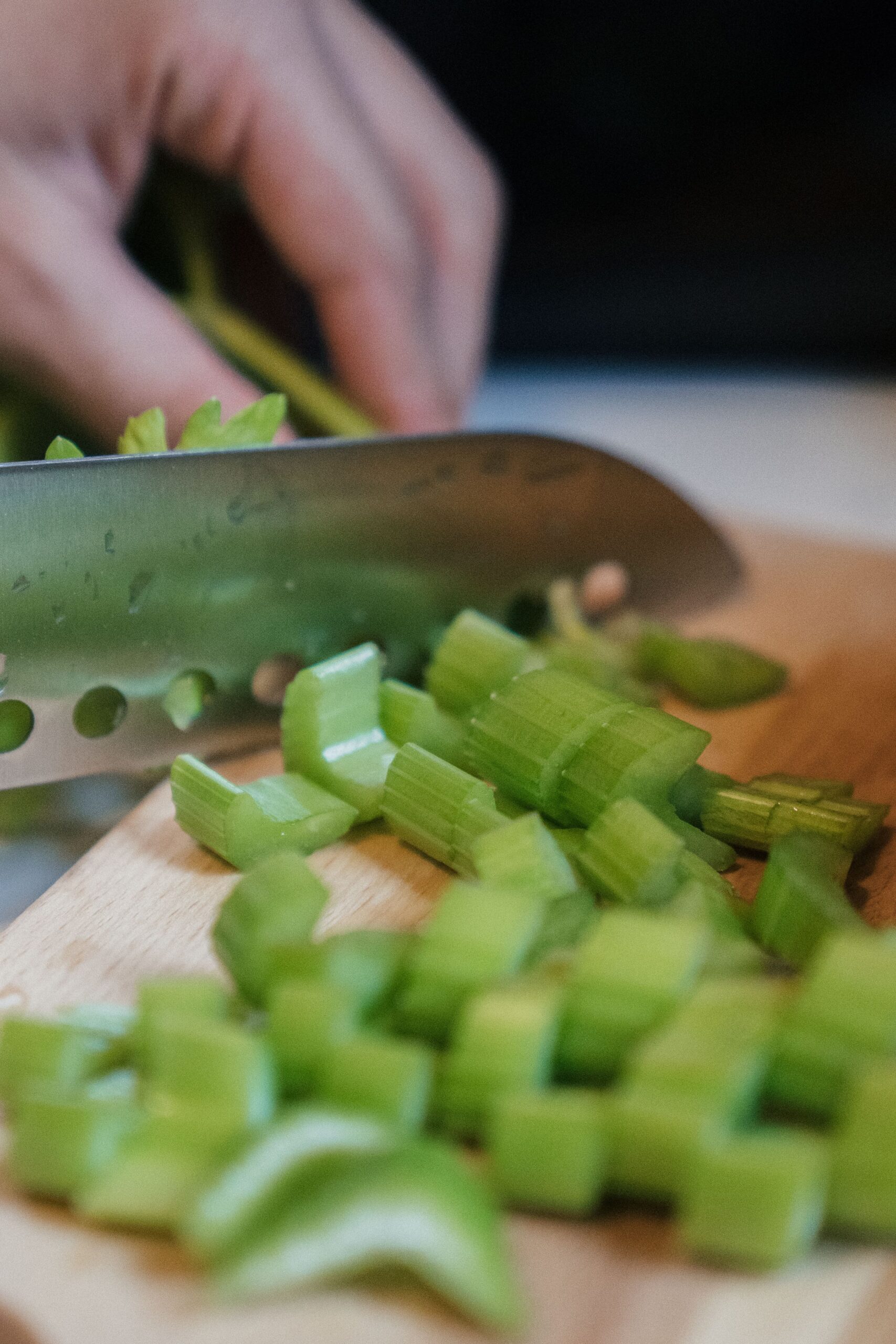 Fresh celery being sliced on a chopping board for chicken noodle soup