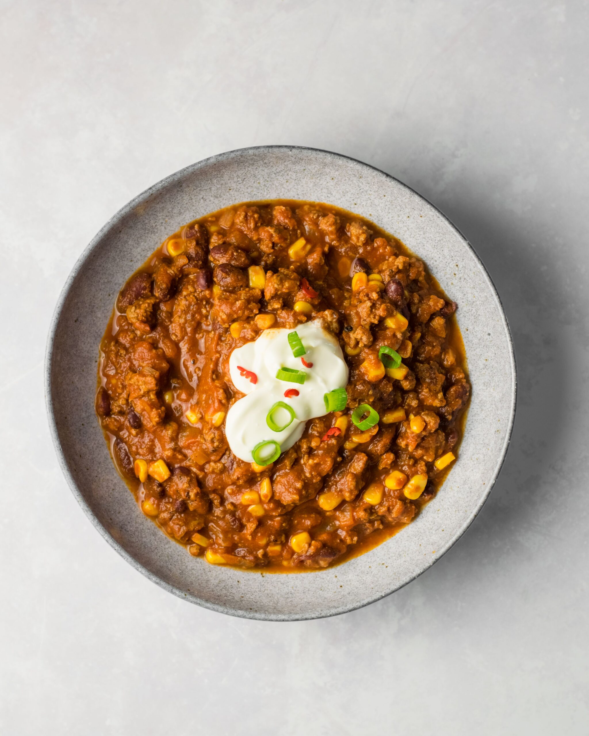 A bowl of classic beef chili with beans, corn and sour cream, top view