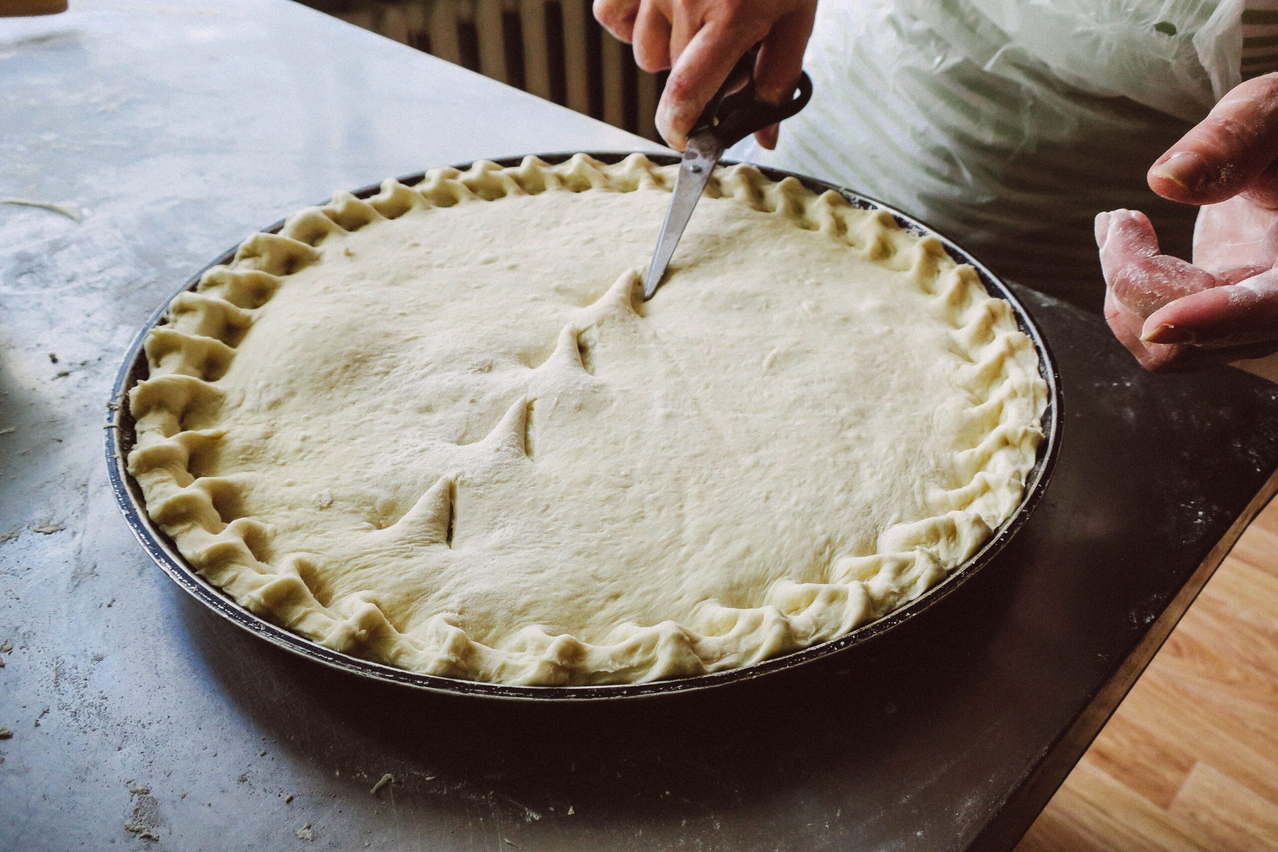Hands crimping the edge of an unbaked chicken pot pie crust before baking