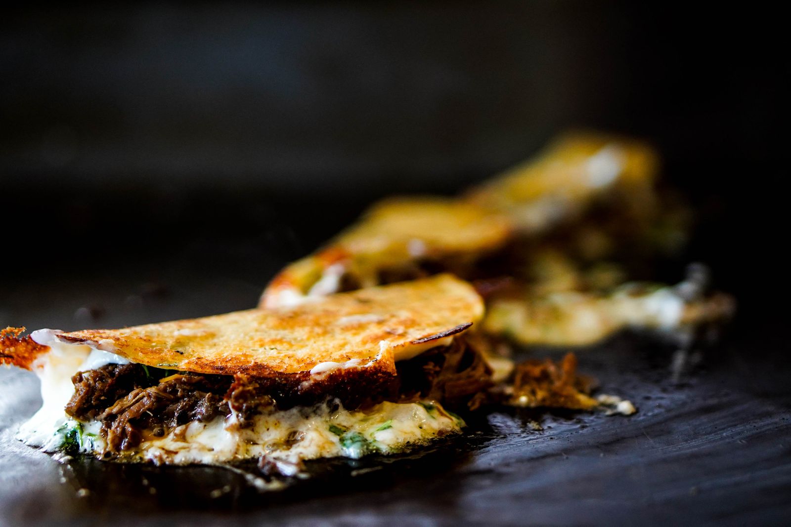 Birria quesabirria tacos crisping on a griddle with melted cheese and shredded beef