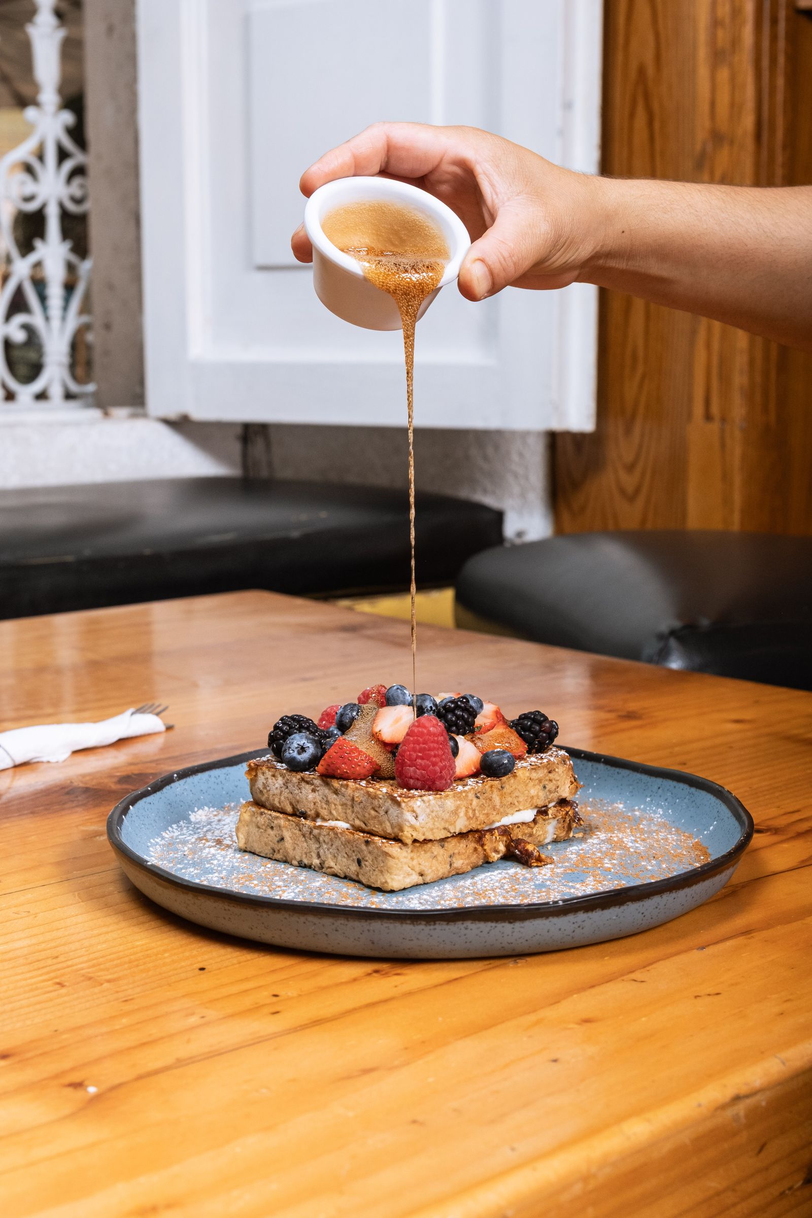 French toast topped with fresh berries and syrup pouring from a dish