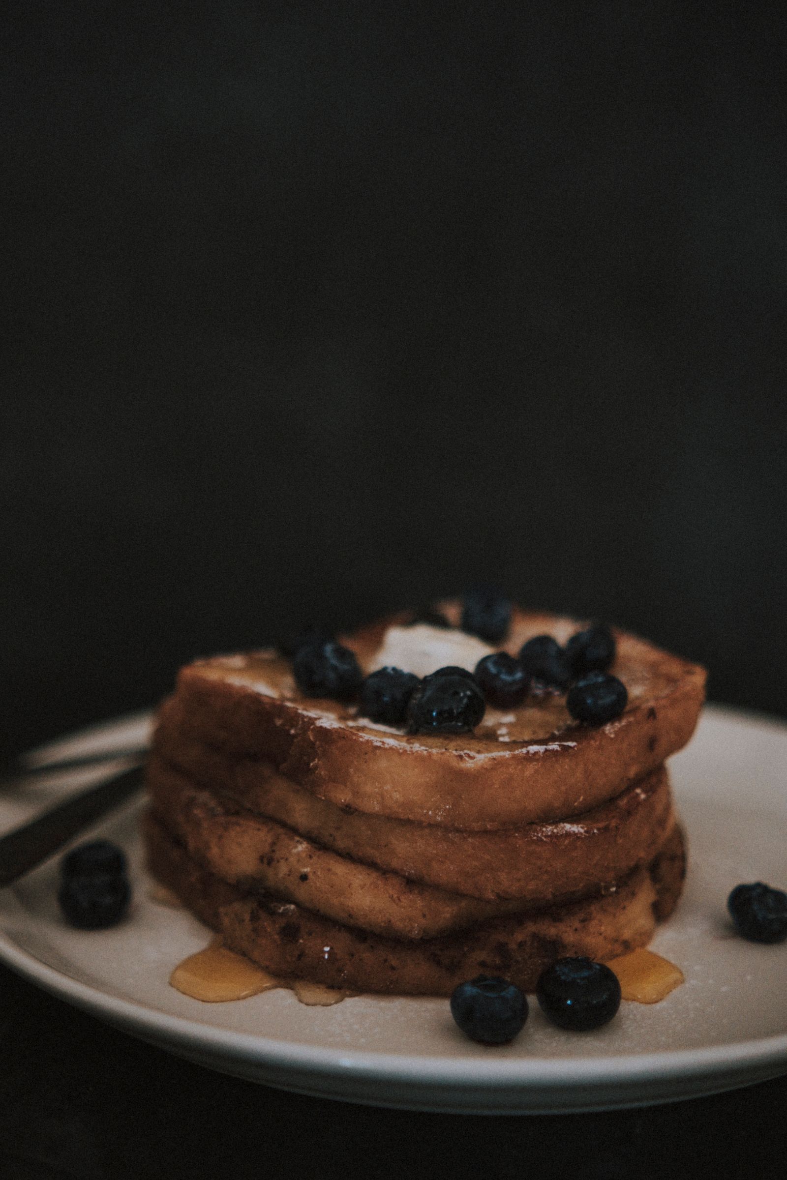 Close-up of syrup drizzled French toast topped with fresh blueberries on a white plate