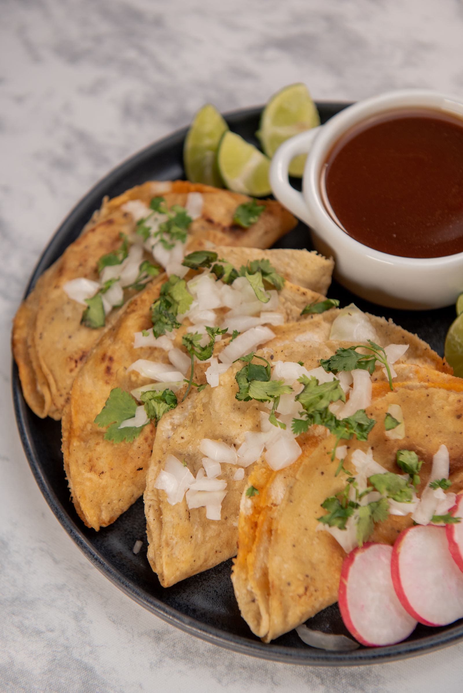 Birria tacos garnished with onion, cilantro and lime wedges
