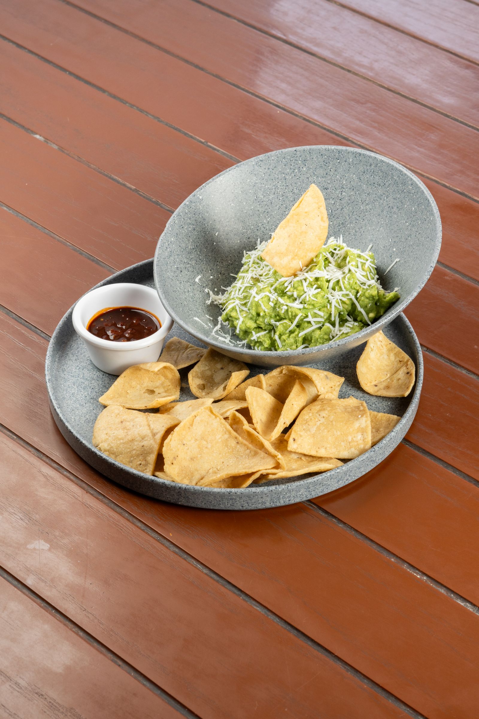 Delicious guacamole with tortilla chips and a side of salsa on a wooden table