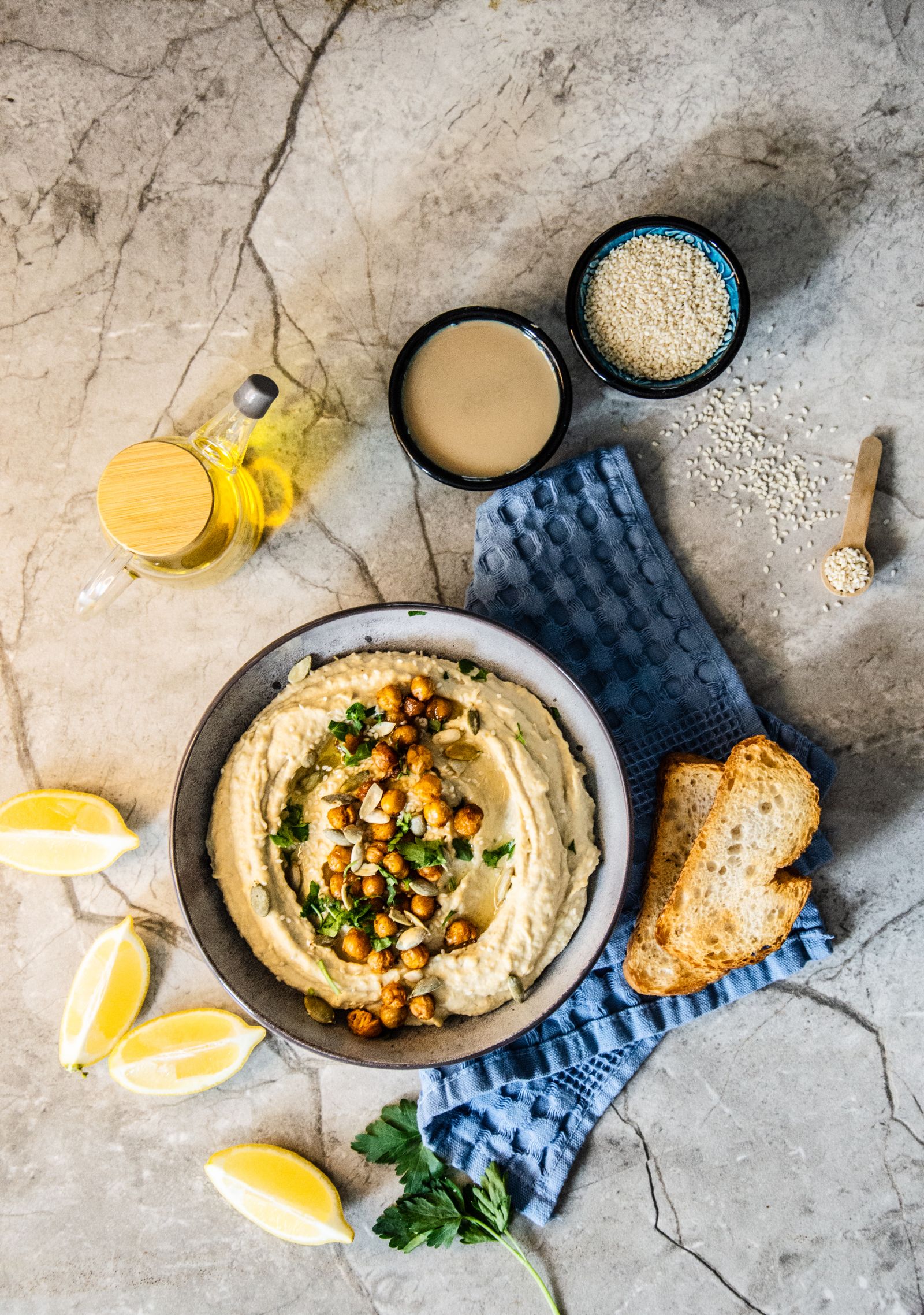 Flat lay of hummus with chickpeas, tahini, olive oil, lemon wedges and bread slices