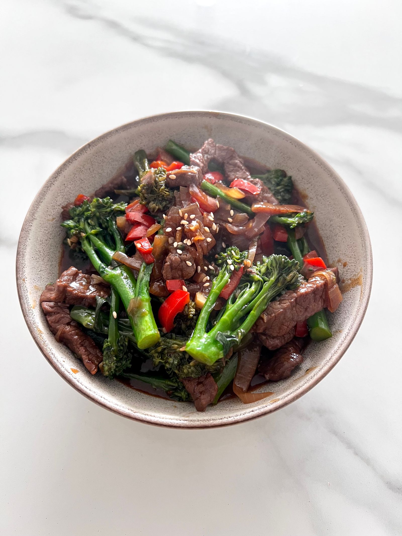 Bowl of beef and broccoli stir-fry with peppers and sesame seeds
