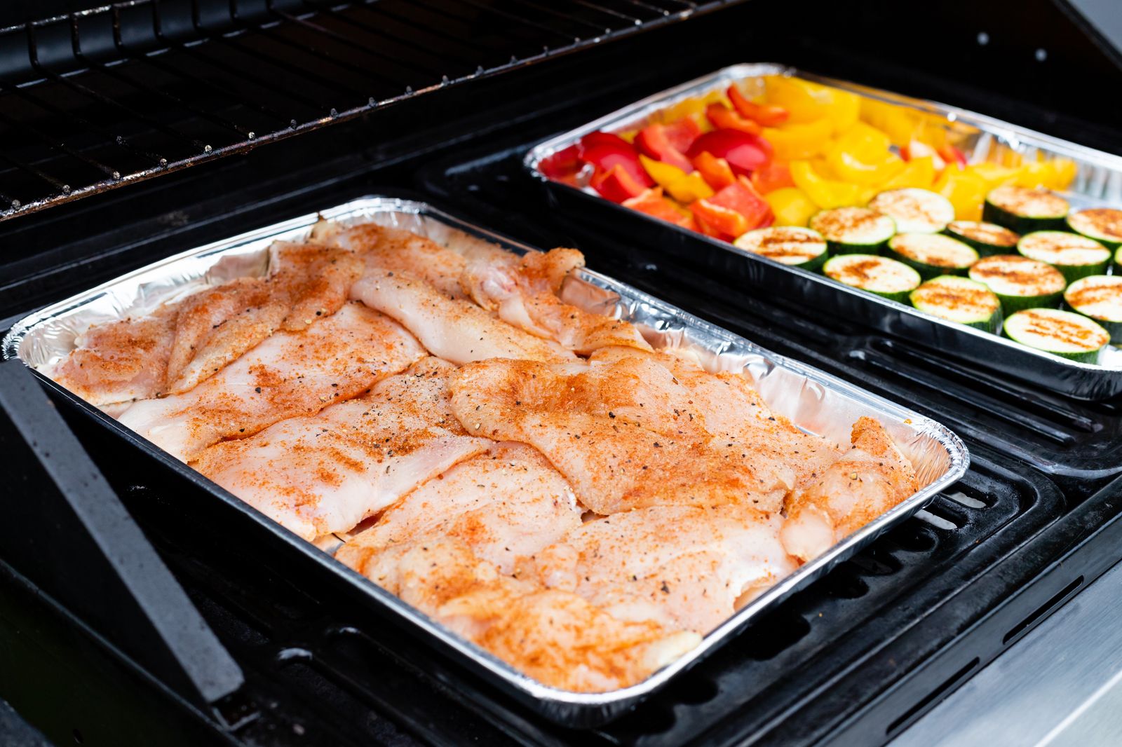Raw seasoned chicken pieces and chopped vegetables arranged on a tray before roasting