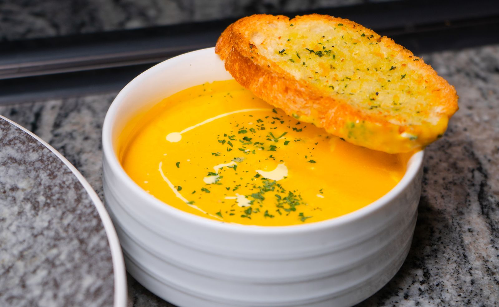 Close up of creamy pumpkin soup garnished with herbs and garlic bread