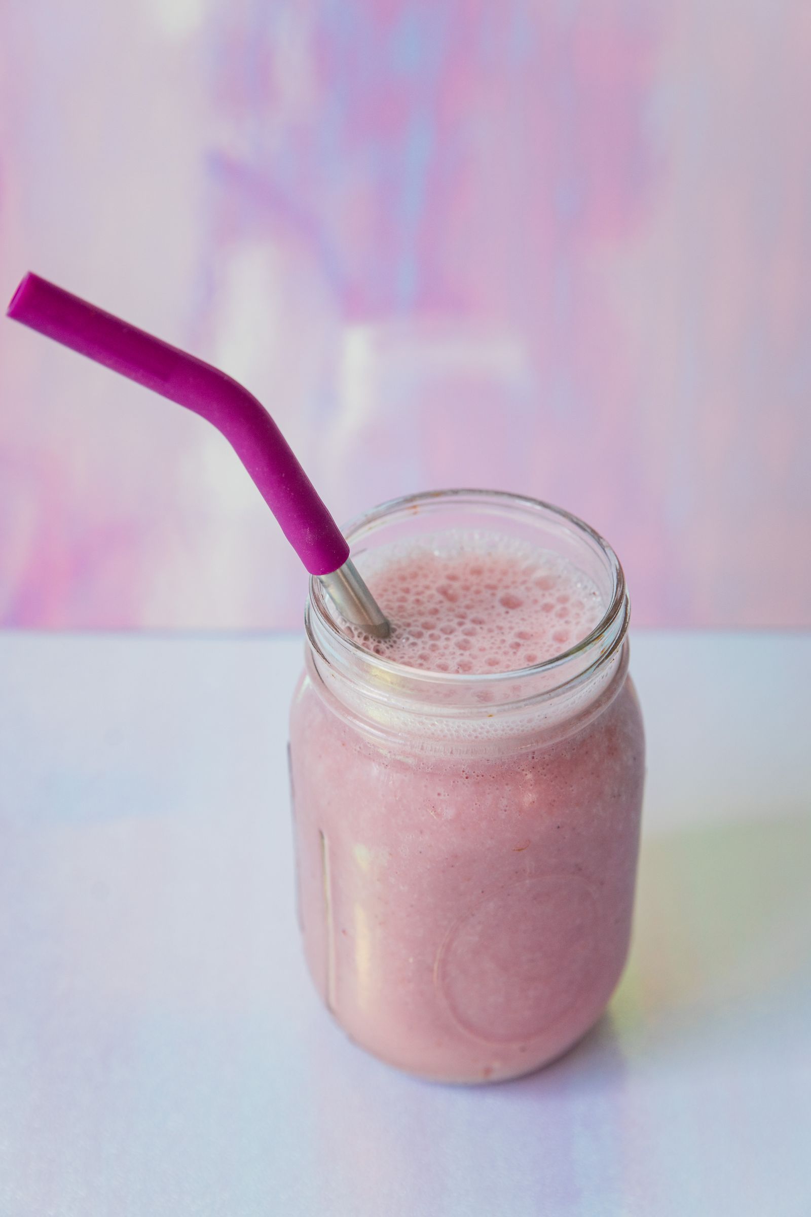 Pink strawberry banana smoothie in a mason jar with a reusable straw