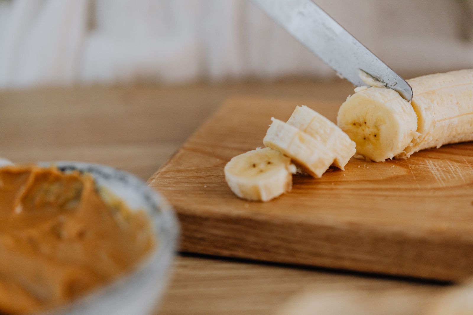 Banana being sliced on a wooden chopping board
