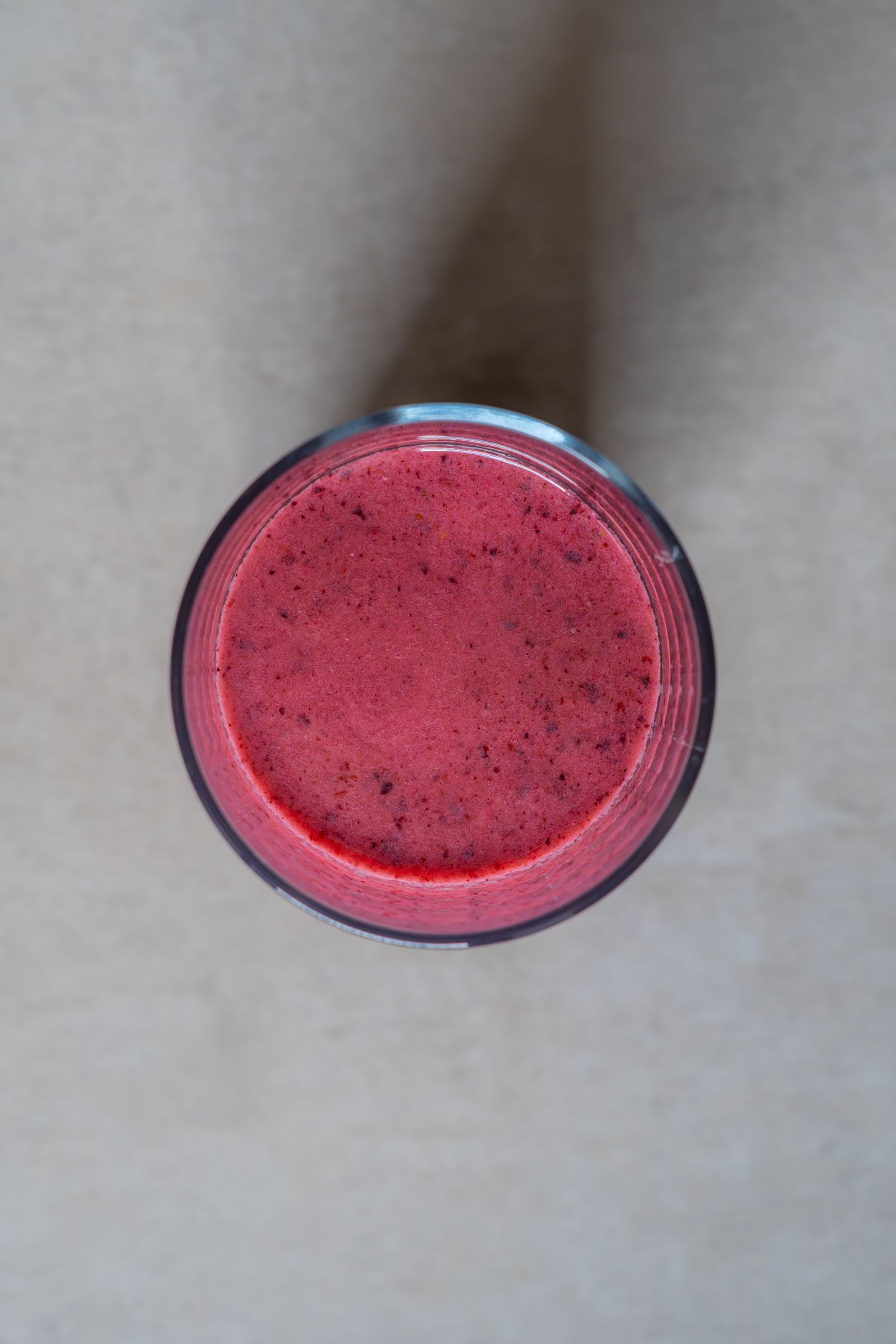 Top-down view of a thick red berry smoothie in a glass