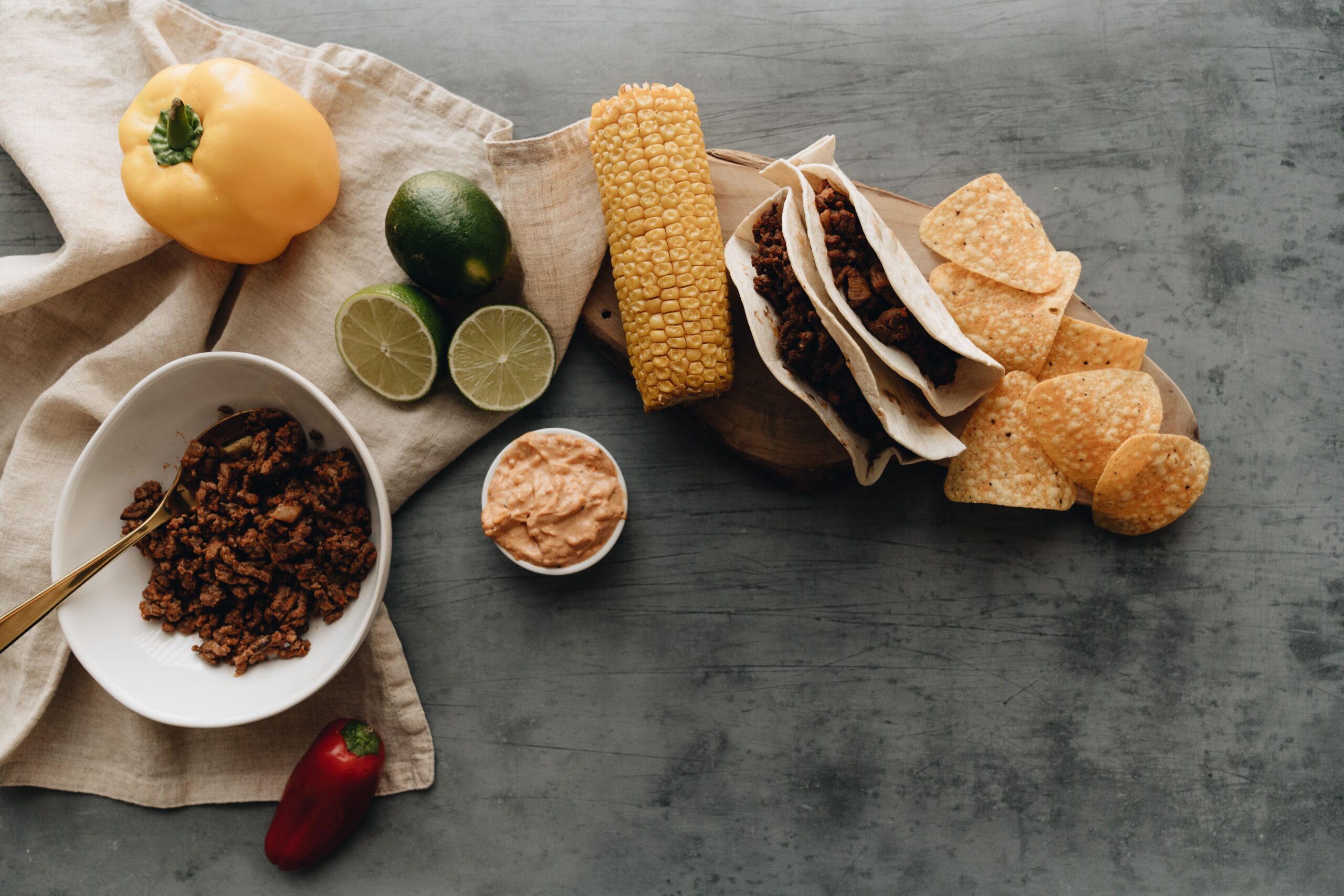 Cooked beef taco filling with toppings, tortillas, corn and tortilla chips laid out