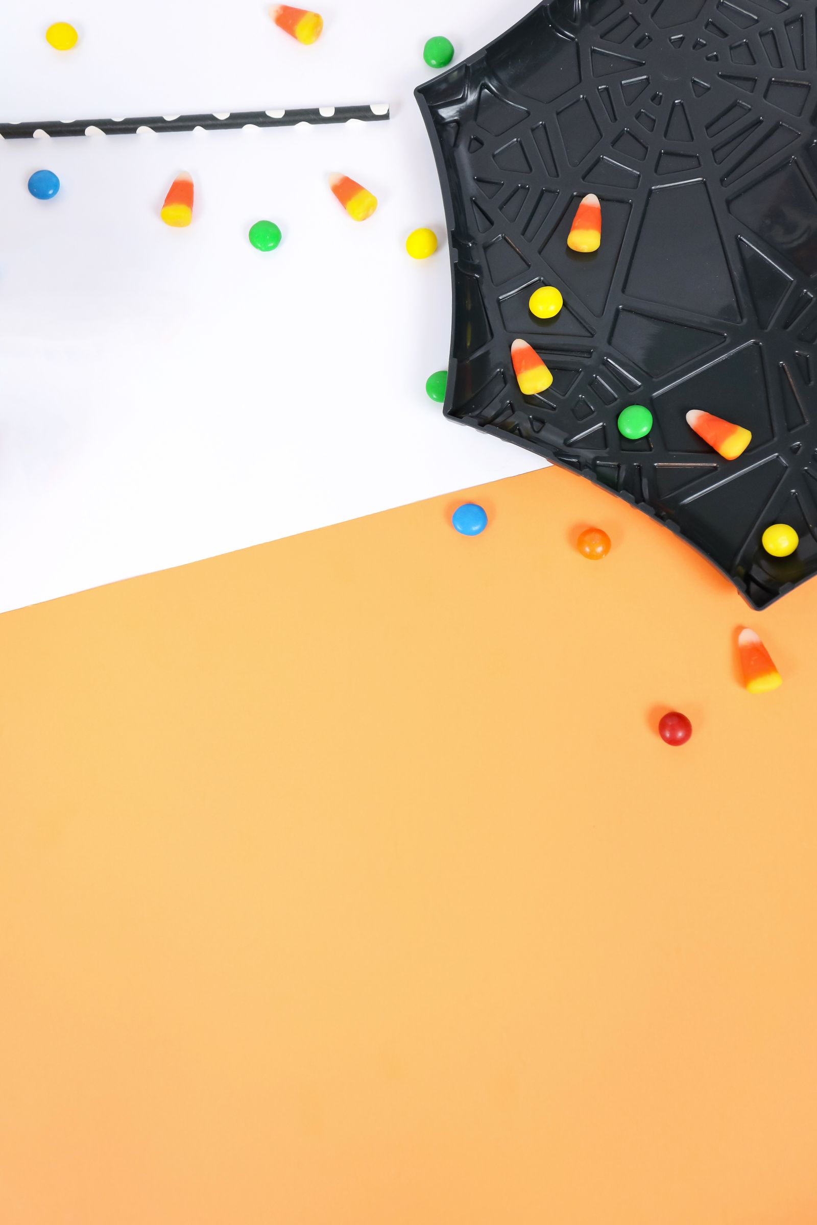 Candy corn and colourful candy pieces scattered on a Halloween themed background