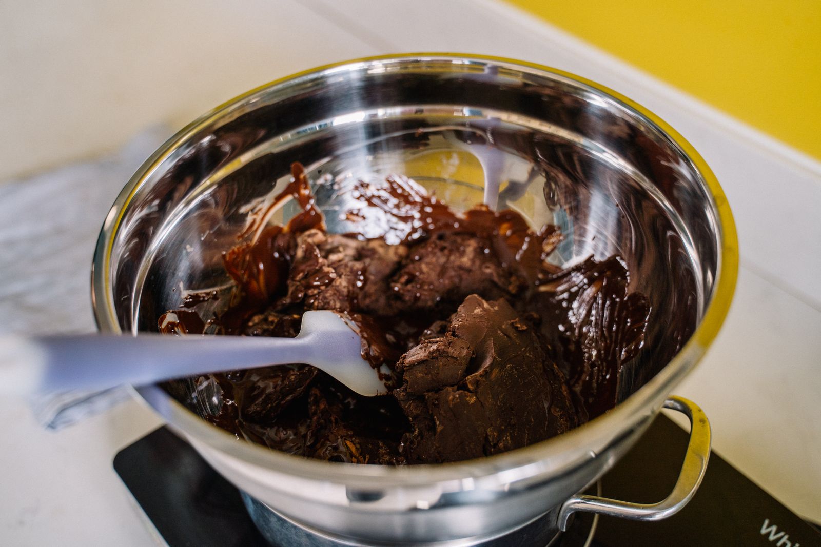 Chocolate melting in a stainless steel bowl, stirred with a spatula