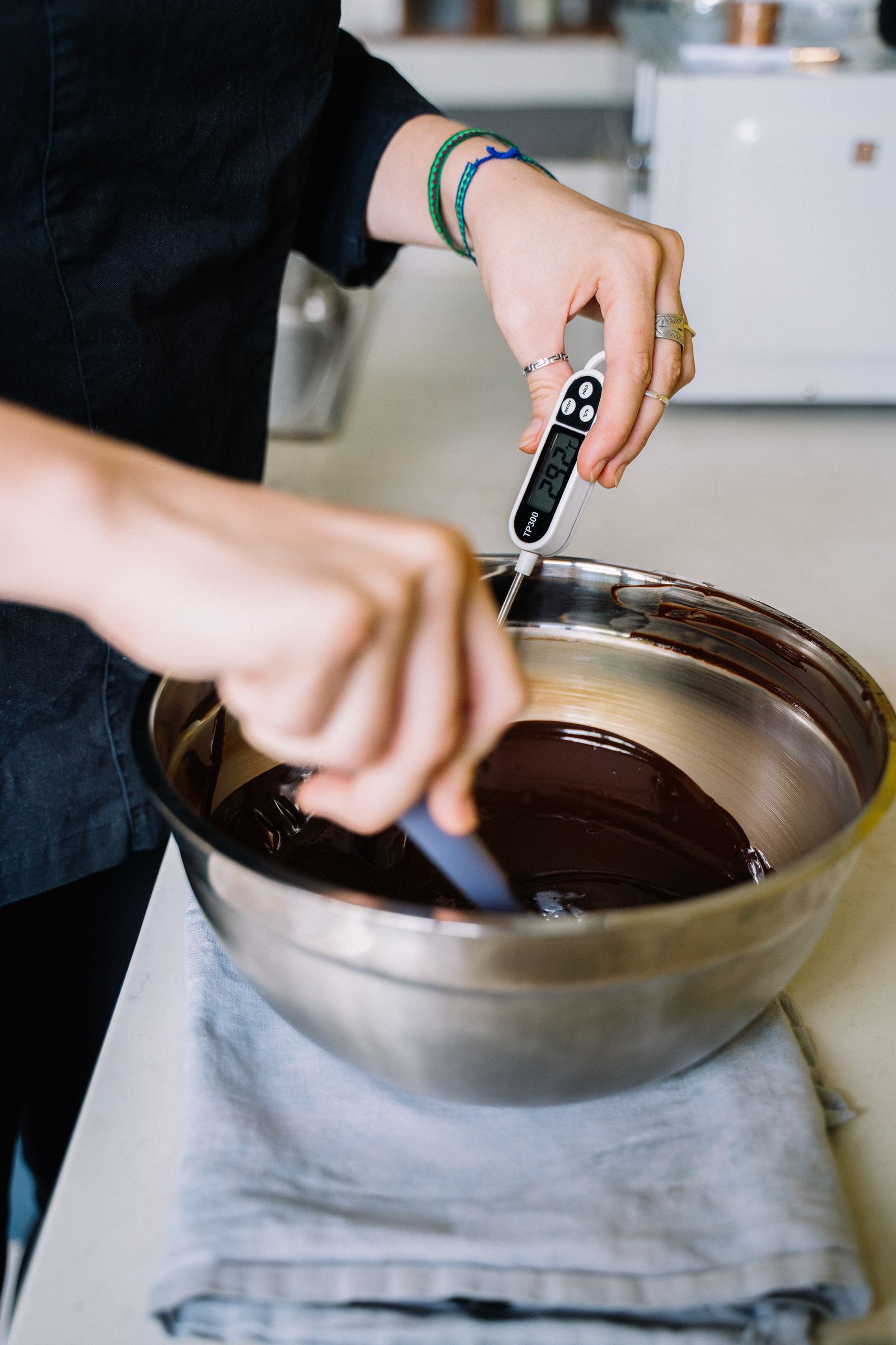 Hands using a digital thermometer to check the temperature of melted chocolate